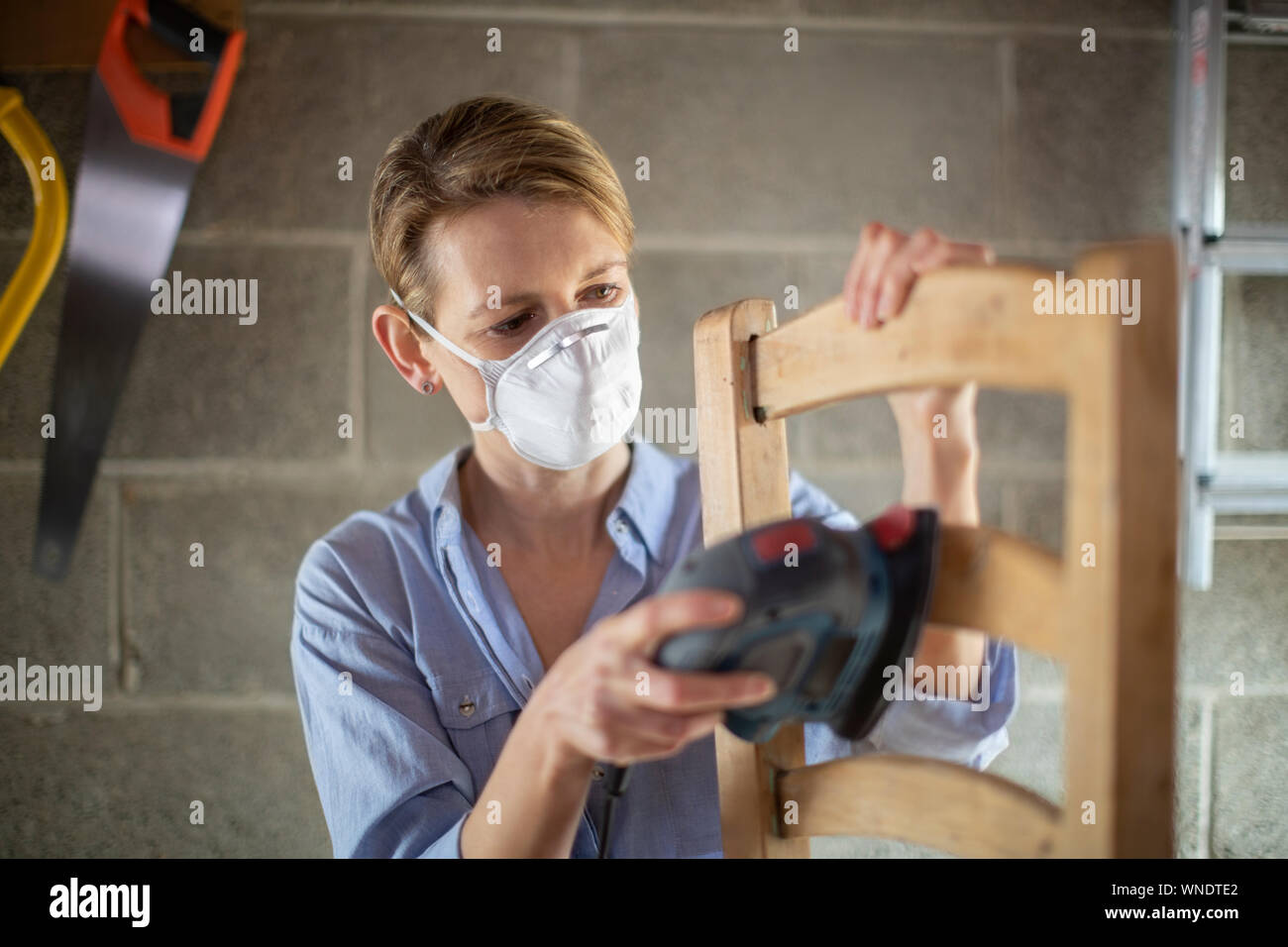 Reife Frau Upcycling Möbel in der Werkstatt zu Hause mit elektrischen Sander Stockfoto