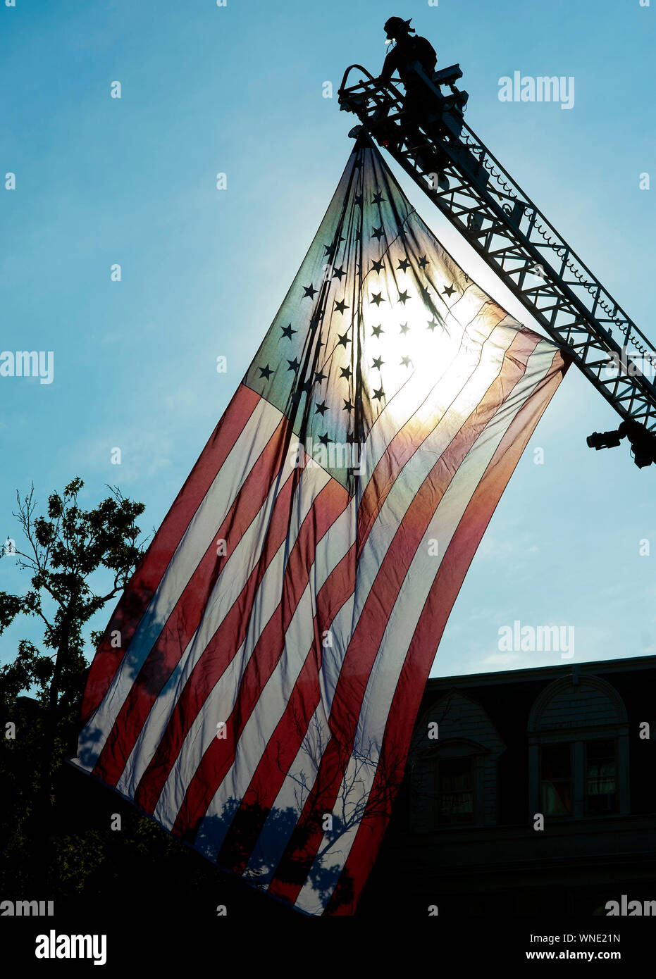 Ein Feuerwehrmann hängt eine große amerikanische Flagge vor dem Beginn einer Zeremonie 9/11 auf dem Global war on Terrorism Memorial Montag, 11. September 2017 im Alter Stockfoto