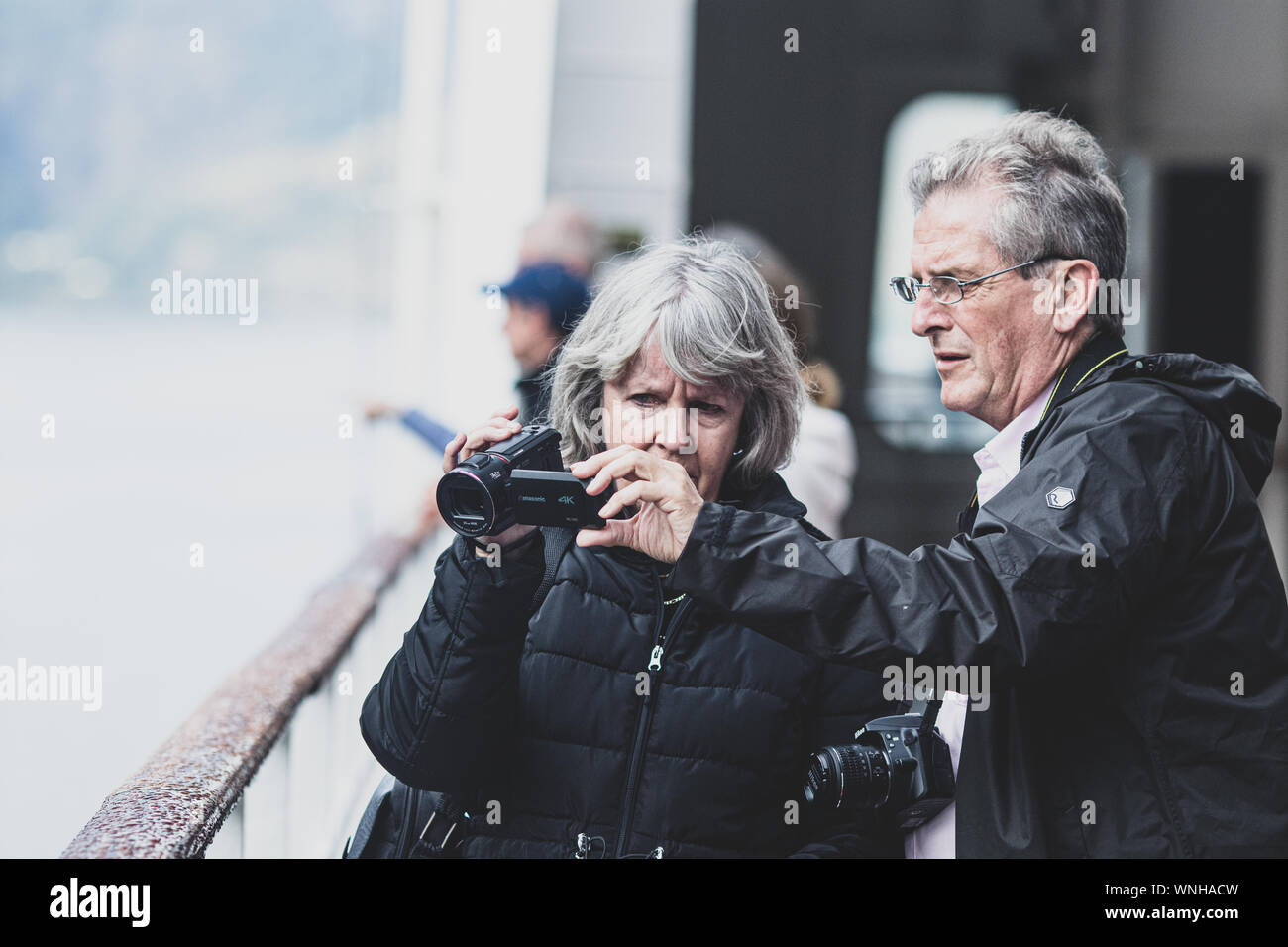 Ein älteres Paar, das ein wenig verwirrt auf ihre Videoeinstellungen auf dem Deck schaut, die Königin Mary 2, während sie auf die schönen norwegischen Fjorde blicken Stockfoto