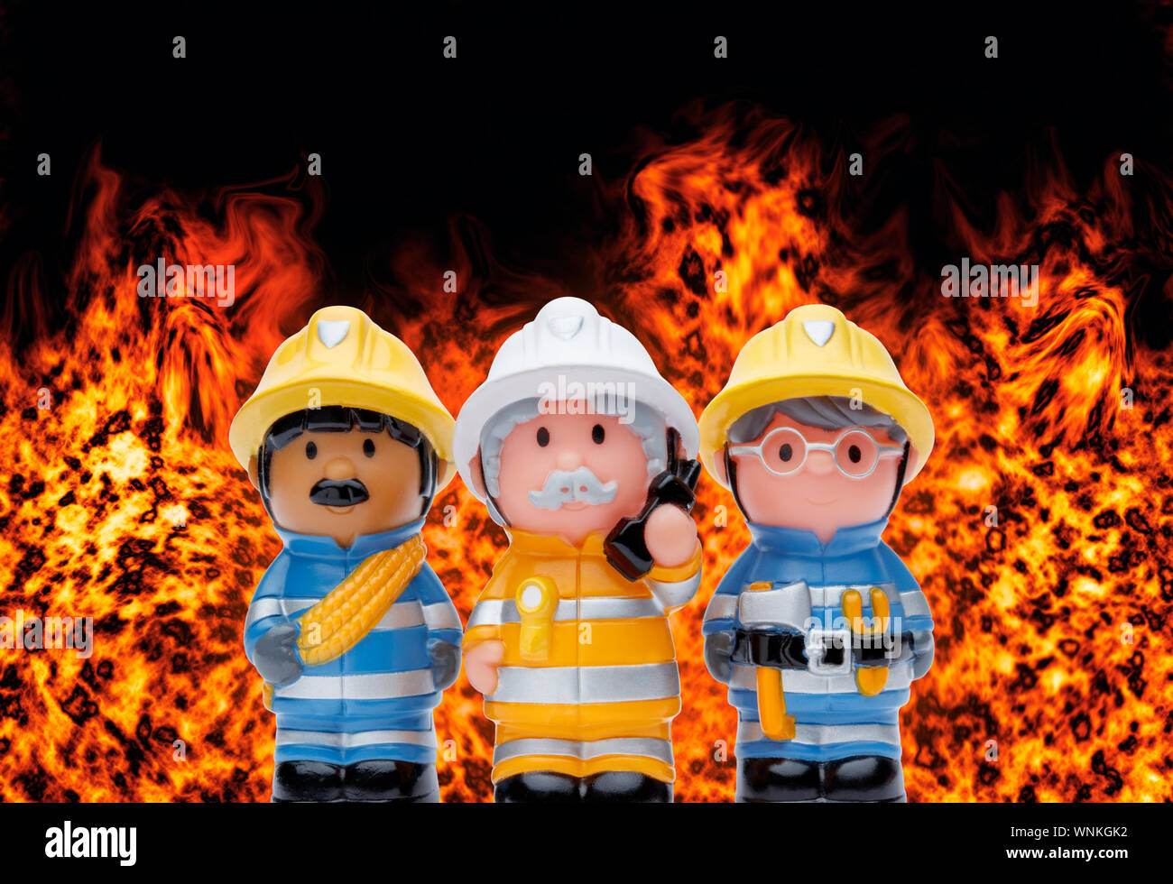 Eine Linie von 3 Spielzeug Feuerwehrmänner ständigen Aufmerksamkeit, mit Flammen brennen im Hintergrund Stockfoto