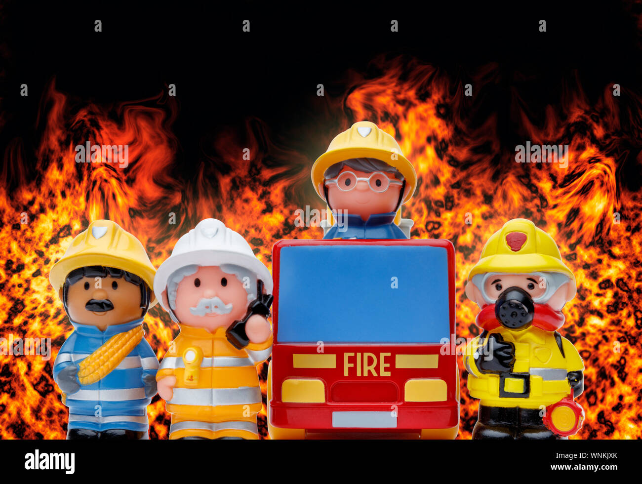 Eine Linie von 3 Spielzeug Feuerwehrmänner ständigen Aufmerksamkeit und ein Feuerwehrauto, mit Flammen brennen im Hintergrund Stockfoto