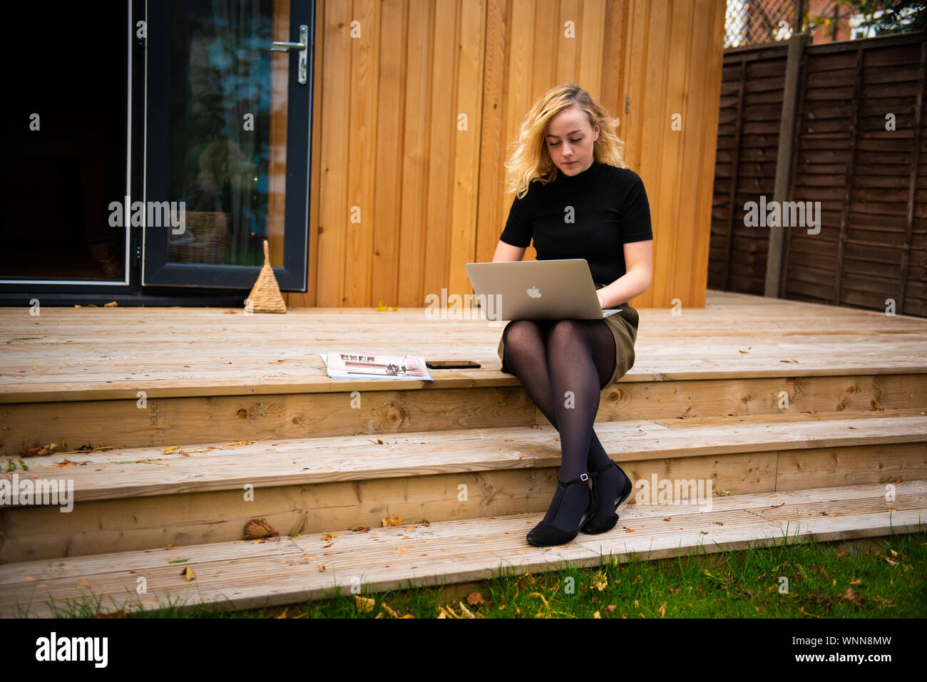 Modell arbeiten von zu Hause auf dem Laptop mit Zedernholz verkleidete Gebäude im Hintergrund Stockfoto