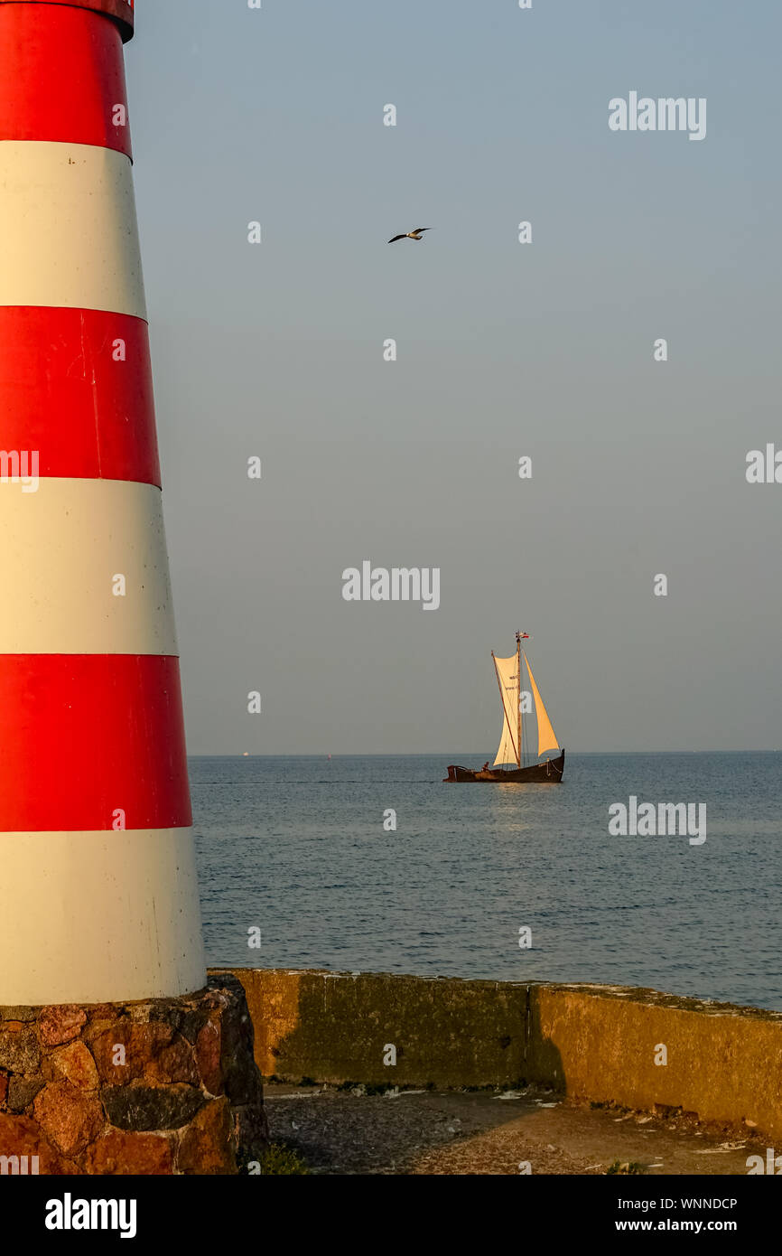 Blick von der Marina mit dem Teil von Leuchtturm auf der linken Seite im Spätsommer. Segelboot in der gemütlichen goldenen Licht des Abends. Ein Vogel fliegt in den Himmel Stockfoto