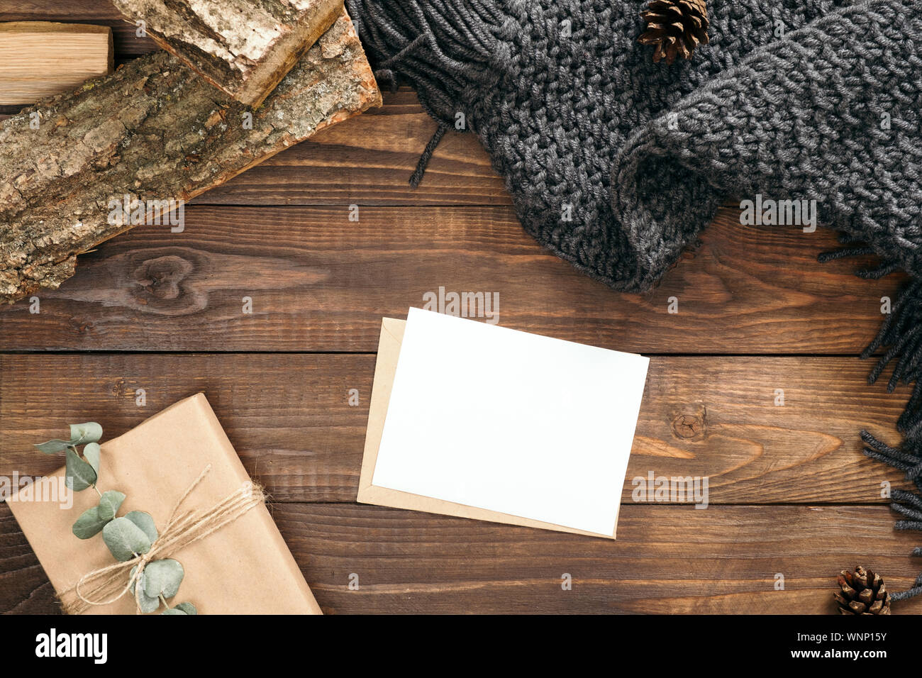 Flatlay gemütlichen Winter oder Herbst Schreibtisch Tisch mit Brief, eine leere Karte, Handwerk Papier Umschlag, Geschenkbox, Strickschal, Brennholz, Holz- Hintergrund. Winter Stockfoto