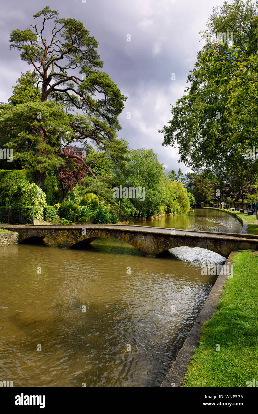 Sonne auf Kiefer und eine Fußgängerbrücke über den Fluss Windrush nach Regen Sturm in Bourton-on-the-Water Village in den Cotswolds England Stockfoto