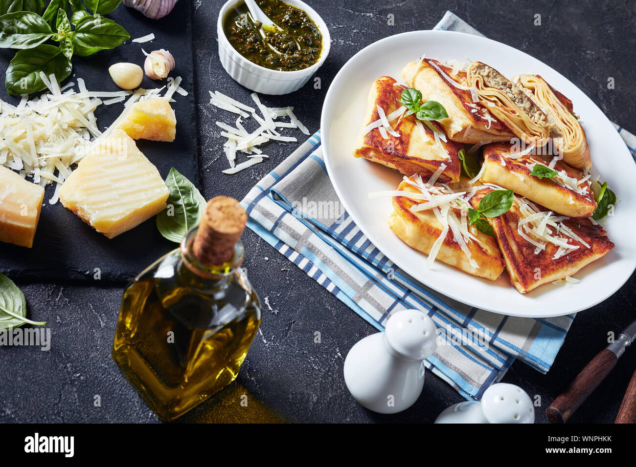 Crepes mit gehacktem Hühnerfleisch auffüllen Crisped in Butter auf einem weißen Teller mit hausgemachten Basilikum sauce Pesto und Zutaten auf eine konkrete Registerkarte serviert. Stockfoto