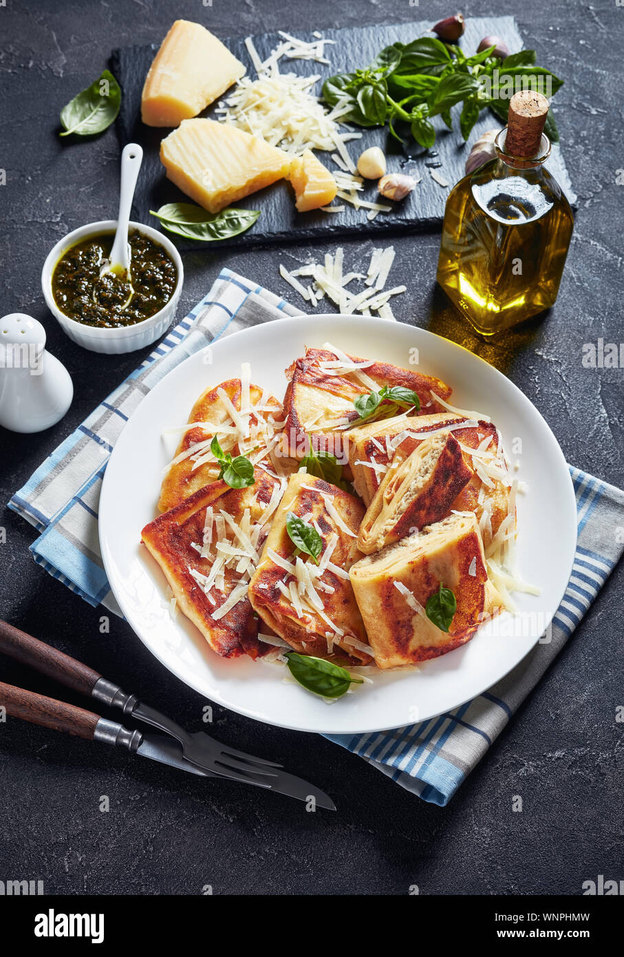 Crepes mit gehacktem Hühnerfleisch auffüllen Crisped in Butter auf einem weißen Teller mit hausgemachten Basilikum sauce Pesto und Zutaten auf eine konkrete Registerkarte serviert. Stockfoto