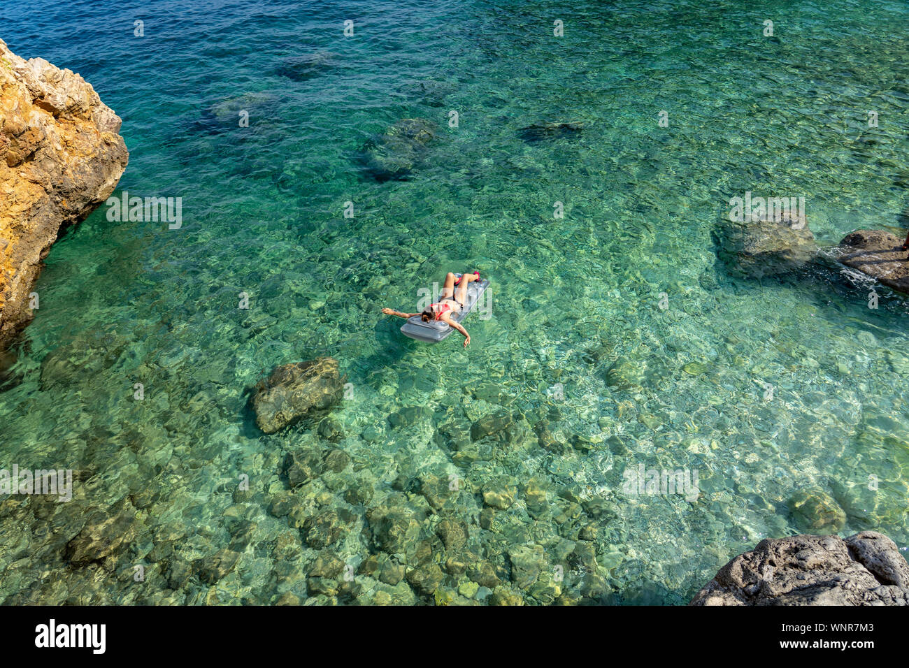 Frau schwimmt auf einer Luftmatratze über das kristallklare Wasser der felsigen malerischen Mali bok orlec natürlichen wilden Strand auf der Insel Cres Kroatien Stockfoto