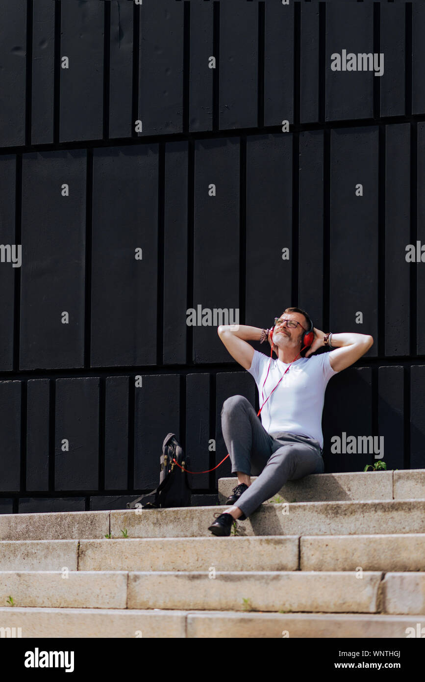 Reifer Mann sitzen auf Schritte mit Kopfhörern und entspannen Sie an einem sonnigen Tag Bärtigen Stockfoto