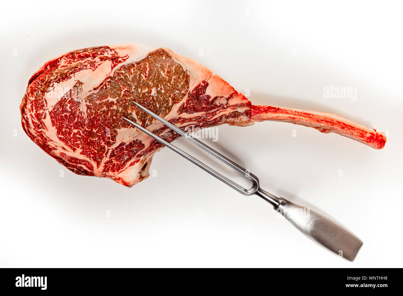 Trocken im Alter von Raw tomahawk Rindersteak auf weißem Hintergrund, Vorderansicht, close-up mit Fleisch Gabel Stockfoto