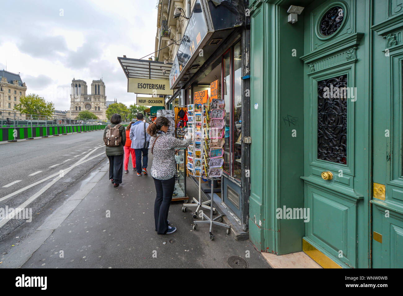 Ein Tourist sucht nach Postkarten in Paris, Frankreich, an einem bürgersteig Souvenirshop am Ufer der Seine mit der Kathedrale Notre Dame in Aussicht Stockfoto