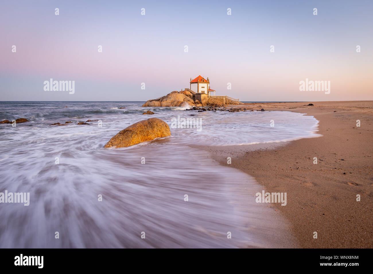 Sonnenaufgang am Strand mit einer Kirche im Meer (Senhor da Pedra Kapelle) Stockfoto