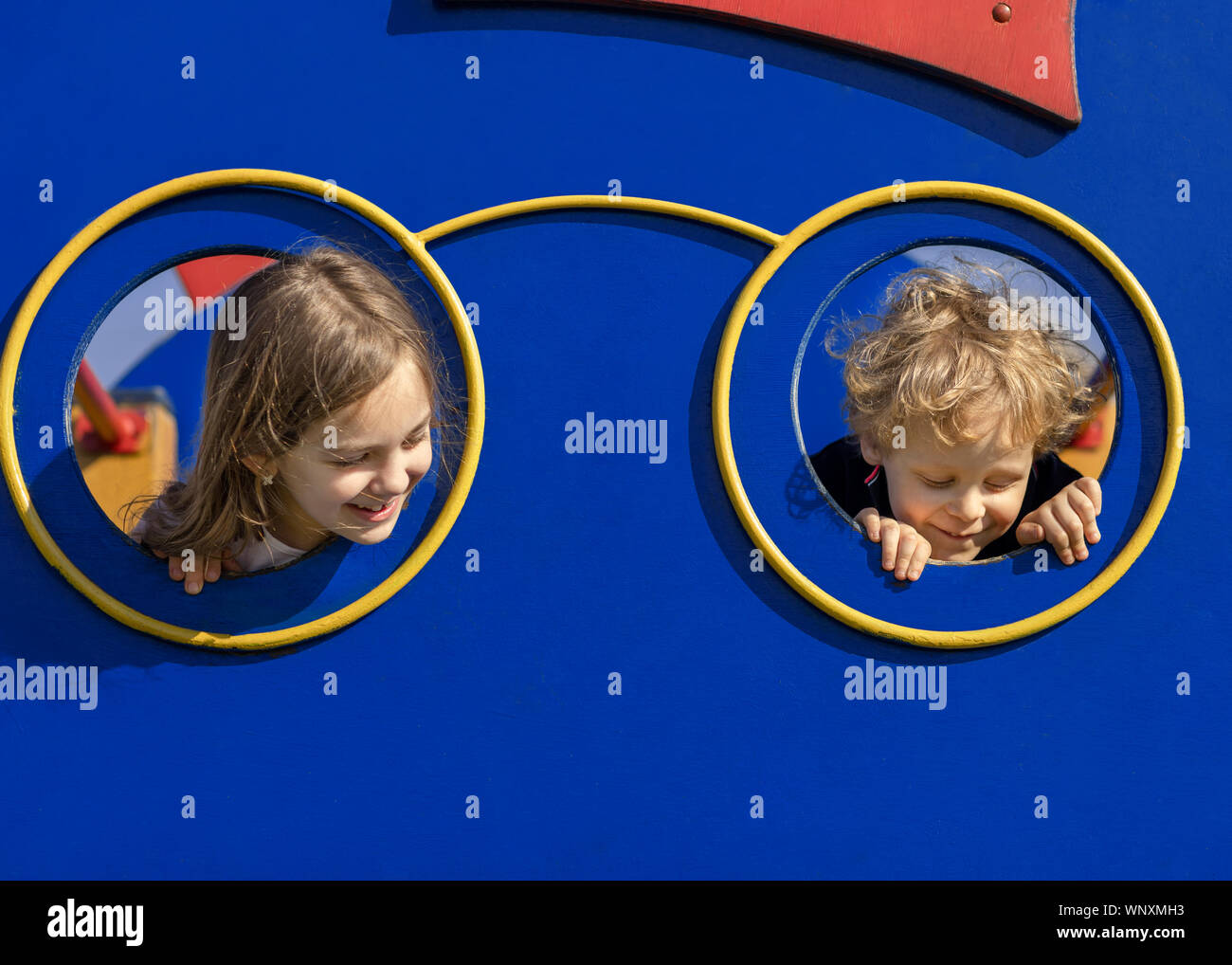 Zwei Kinder spähen durch die Öffnung im Spielhaus. Junge und Mädchen spielen im Park. Glückliche Kinder Konzept. Stockfoto