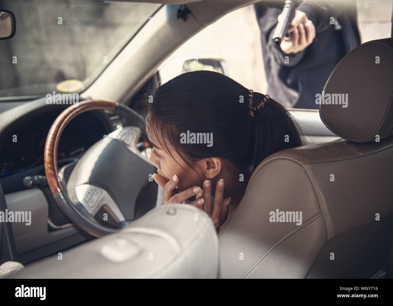 Asiatische junge Frau Angst im Auto mit Räuber in Schwarz gekleidet, und zeigen Sie mit einem Gewehr auf eine Frau Fahrer in einem Auto. Gefährlicher Mann Raub Auto, Angst, m Stockfoto