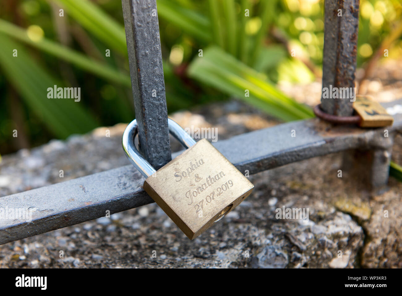 Messing Vorhängeschloss oder Liebe Sperren mit den Namen von ein paar an den schmiedeeisernen Bar von einem Zaun in der Nähe zu sehen, befestigt Stockfoto