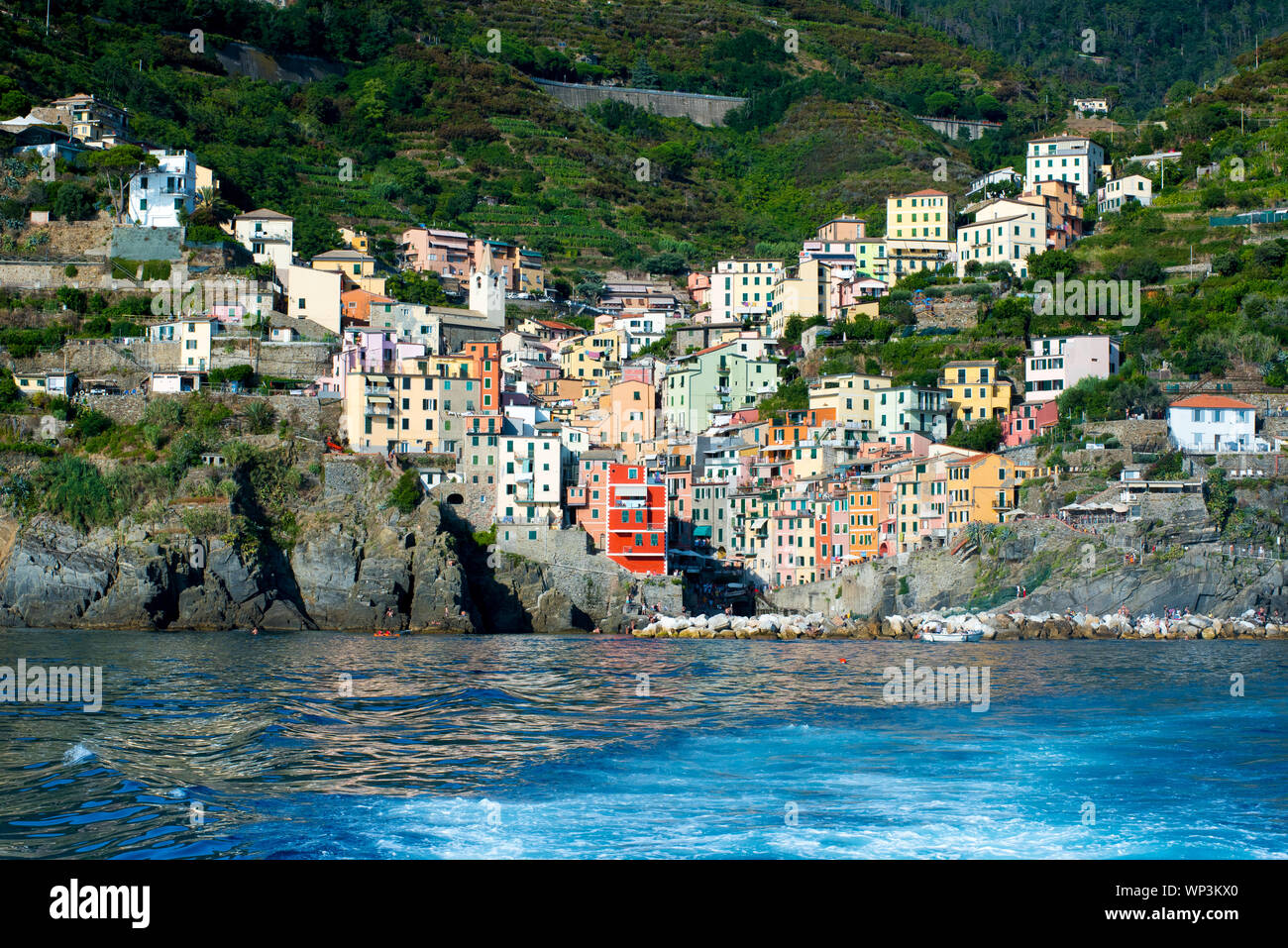 Blick auf die farbenfrohe Architektur der populären Riomaggiore, Cinque Terre, Ligurien, Italien vom Meer mit einem Kreuzfahrtschiff oder Fähre in der foregro Stockfoto