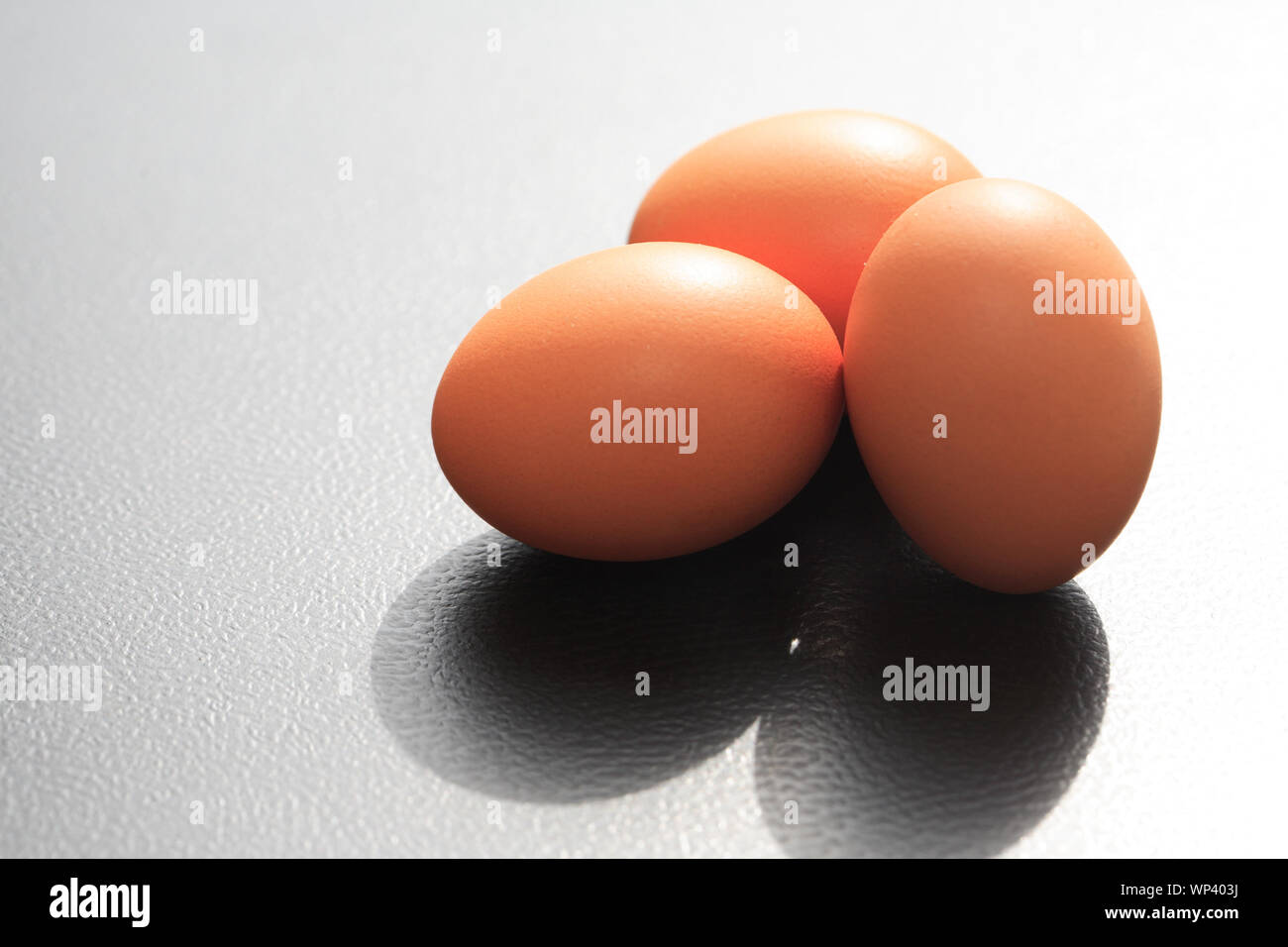 Drei Hühnereier auf schwarzem Hintergrund gegen Morgen Sonne Licht Stockfoto