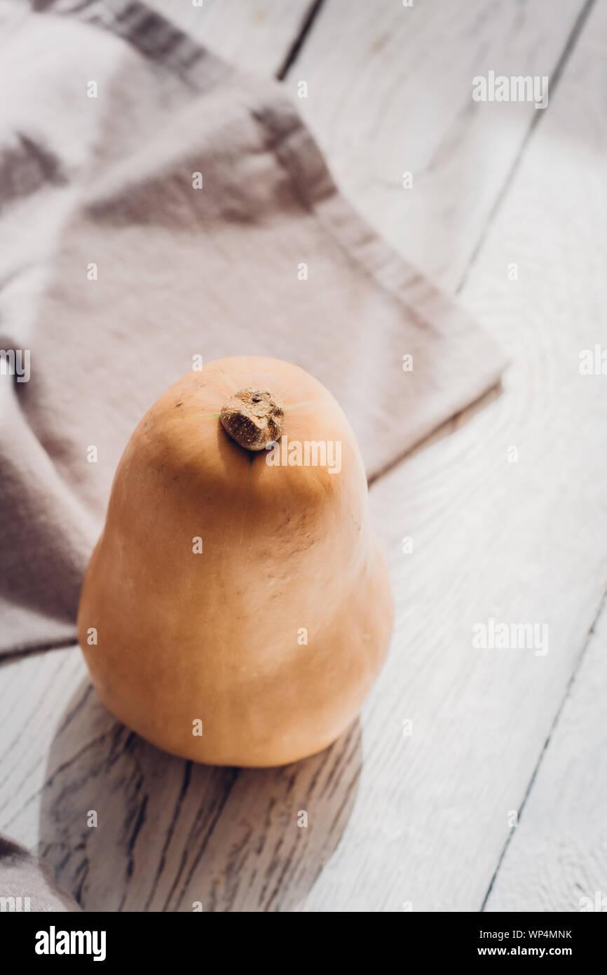 Ein kleiner butternut mit Bettwäsche Küche Handtuch auf weißem Holz- Hintergrund. Herbst saisonal noch leben, fallen Minimalismus blogging Konzept. Der leere Raum fo Stockfoto