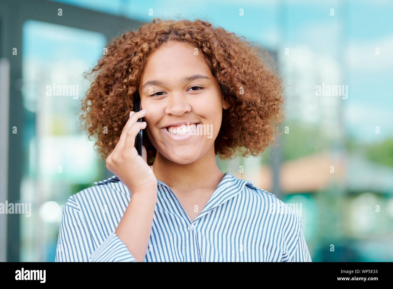Junge fröhliche Geschäftsfrau mit dem lockigen braunen Haar sprechen auf dem Smartphone Stockfoto