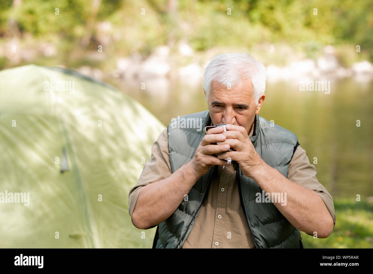 Ältere Wanderer mit grauen Haaren trinken heißen Tee von touristischen Tasse während Rest in Stockfoto