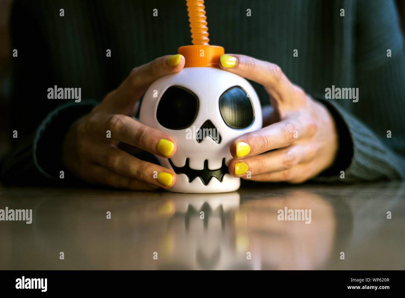 Anonyme Hände mit Maniküre halten Sie eine Tasse mit einem Schädel in Halloween Stockfoto