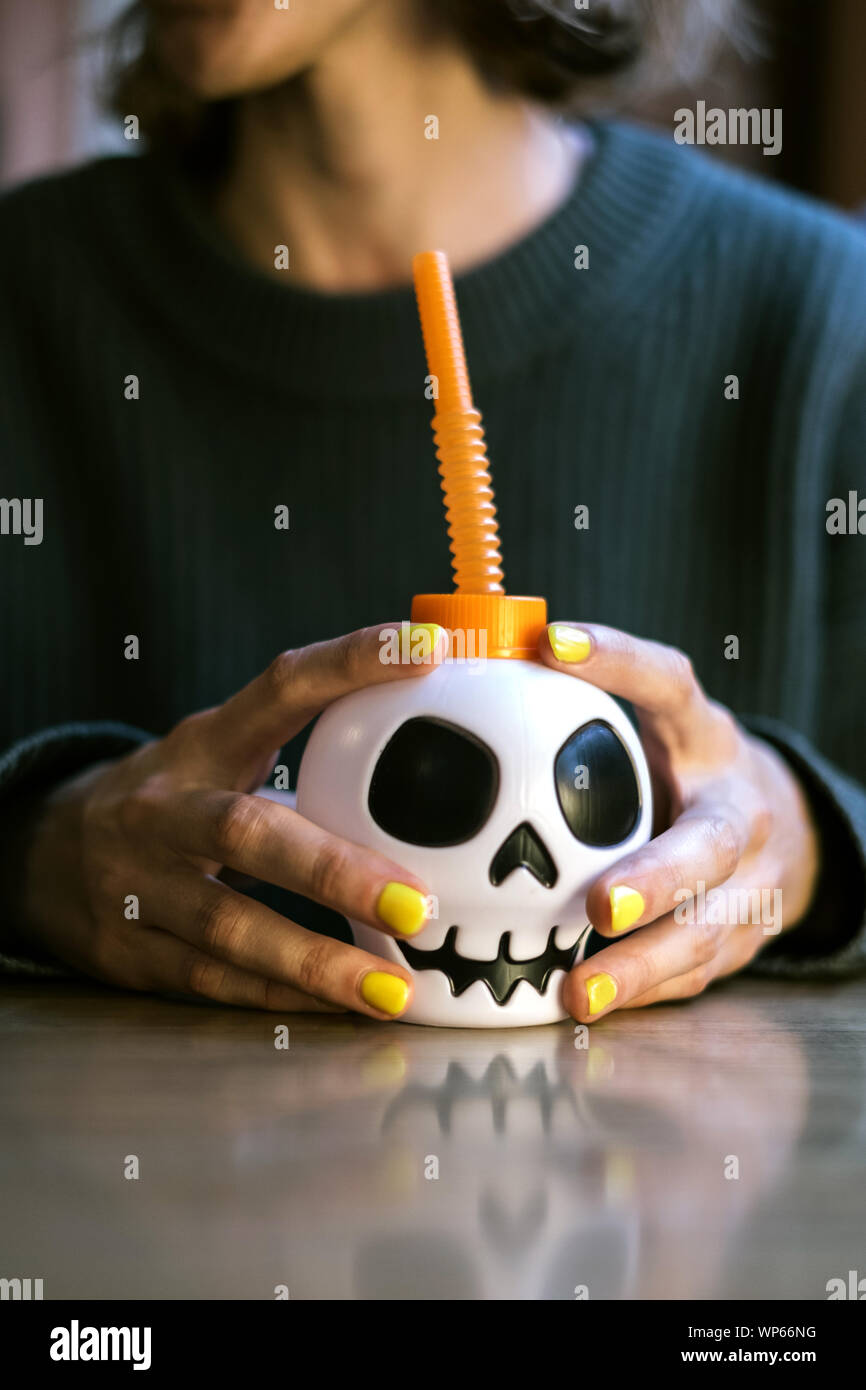 Anonyme Hände mit Maniküre halten Sie eine Tasse mit einem Schädel in Halloween Stockfoto