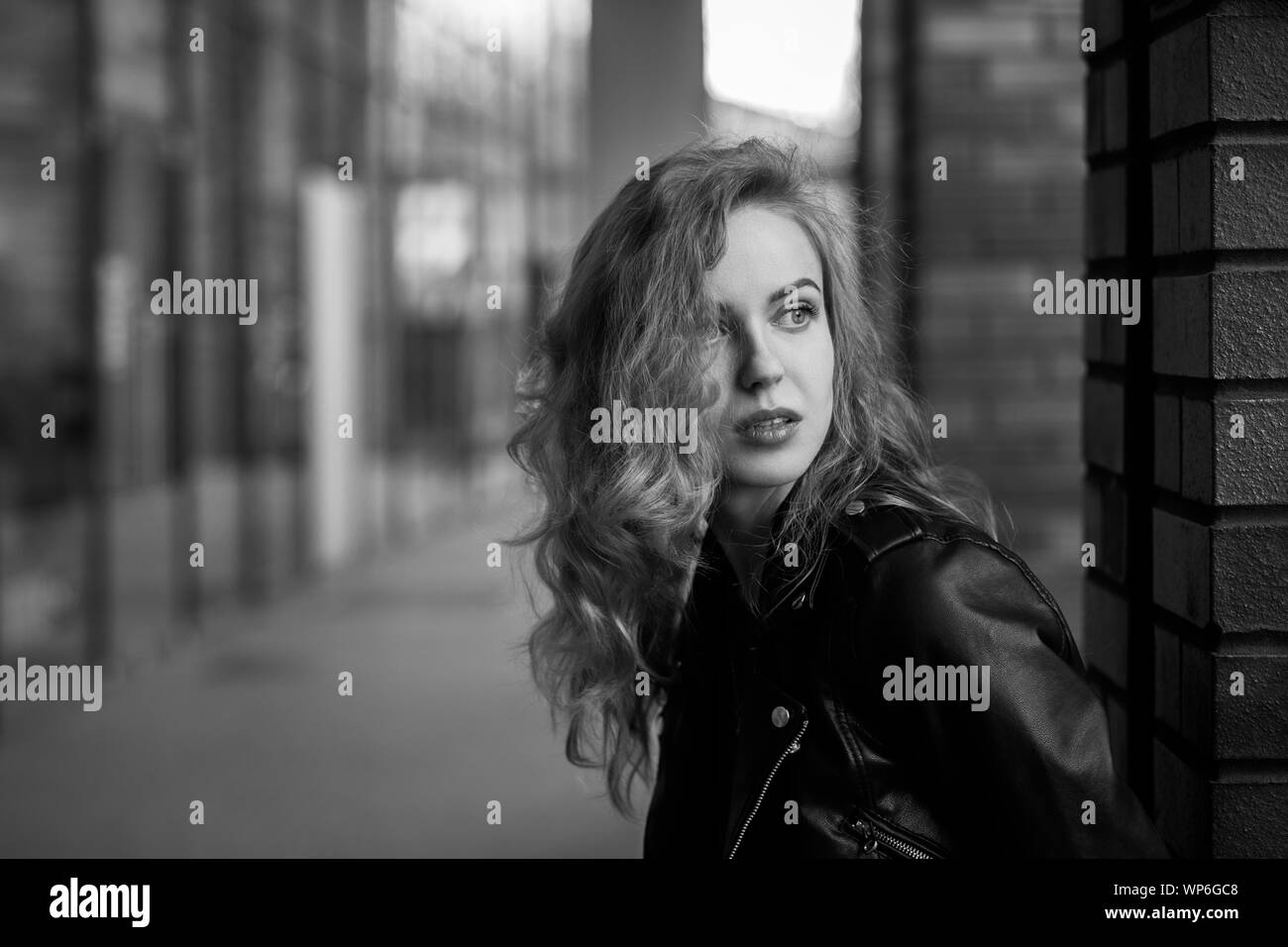 Attraktive curly blonde Mädchen in Lederjacke auf der Straße der Stadt, die von der Kamera über die Schulter, Monochrom Stockfoto