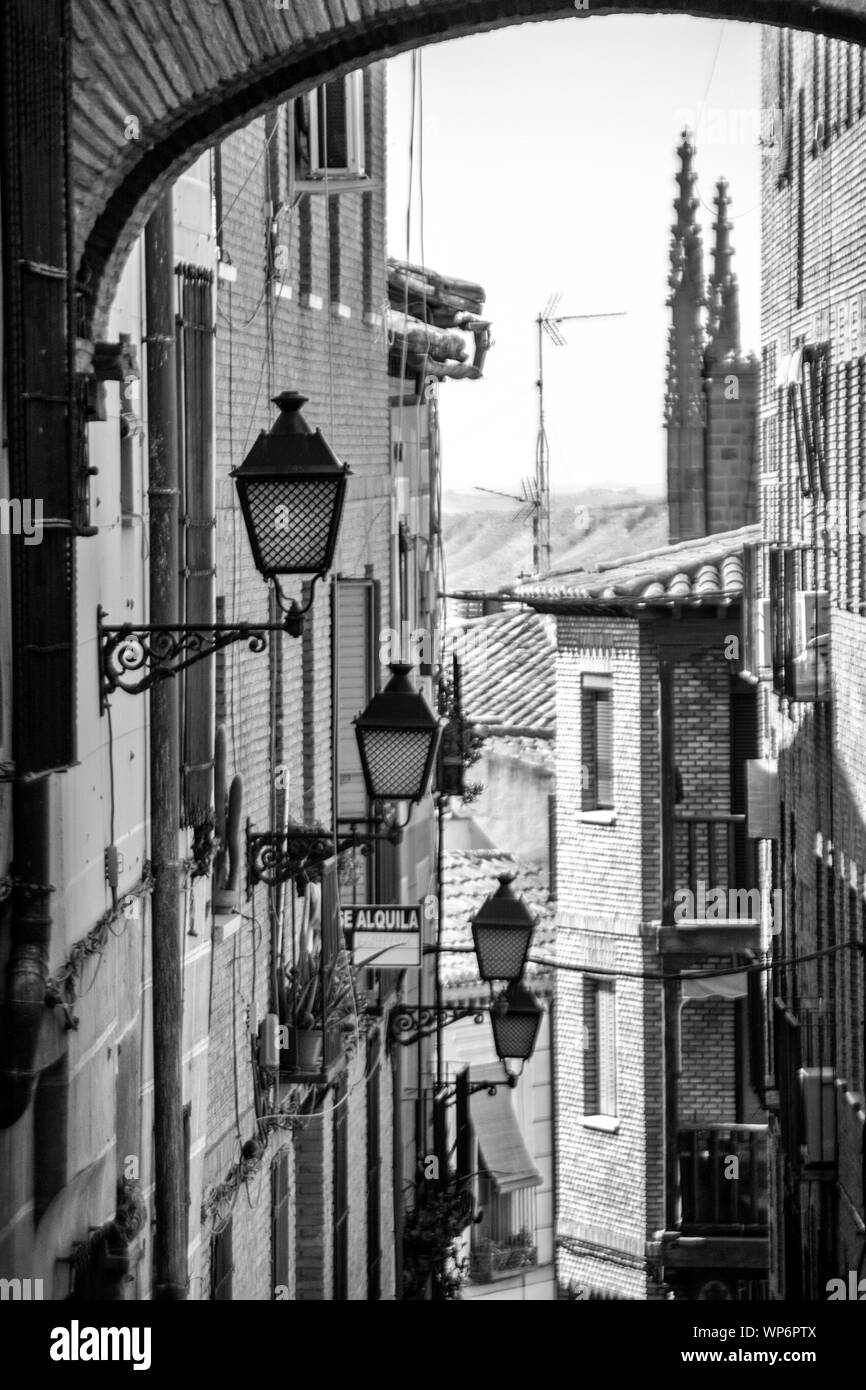 Schwarz-Weiß-Bild von Straßenlampen an einer Wand montiert, durch einen Bogen gesehen, Toledo, Spanien. Stockfoto