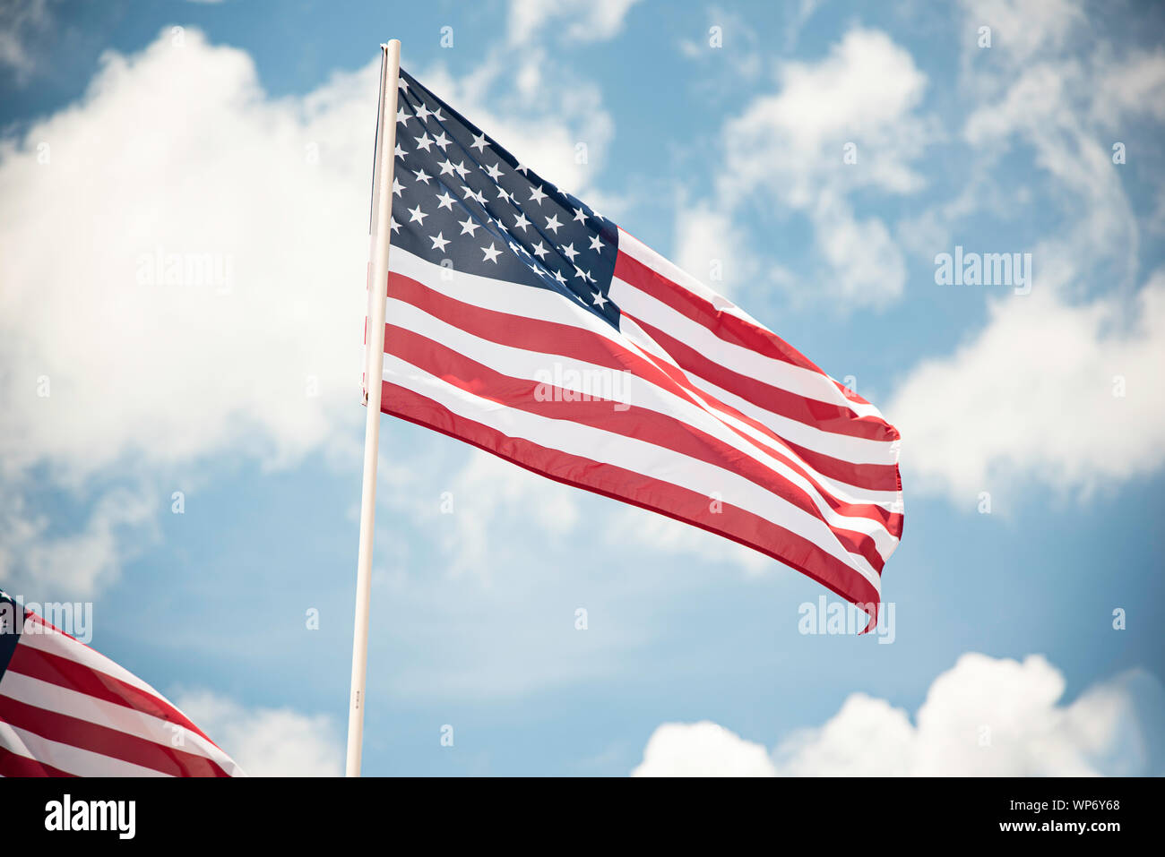 Zwei amerikanische Flaggen im Wind flattern vor einem strahlend blauen Himmel mit flauschigen weissen Wolken. Stockfoto