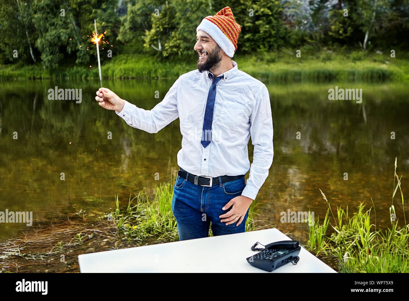Ein Büroangestellter hält eine brennende Wunderkerze in der Hand während einer Firmenfeier. Weißer Kragen in einem lustigen Hut eines Gnome, oder Santa Claus, während der Cel Stockfoto