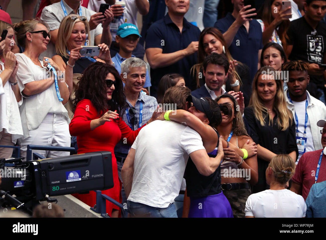 Flushing Meadows, New York, Vereinigte Staaten - 7. September 2019. Bianca Andreescu umfasst Unterstützer und Mitglieder ihres Teams als Eltern an im roten Kleid und Plaid Shirt Aussehen auf, Momente nach dem Sieg über Serena Williams die Damen Einzel Titel bei den US Open heute zu erfassen Links hören. Stockfoto