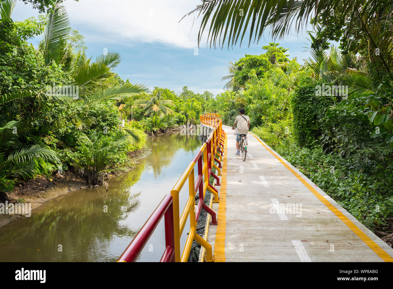 Ein junger Mann (Krachao Zyklen in Bang Bang Kachao), entlang der Wassergraben und Gestelzt weg von üppiger tropischer Vegetation umgeben. Stockfoto