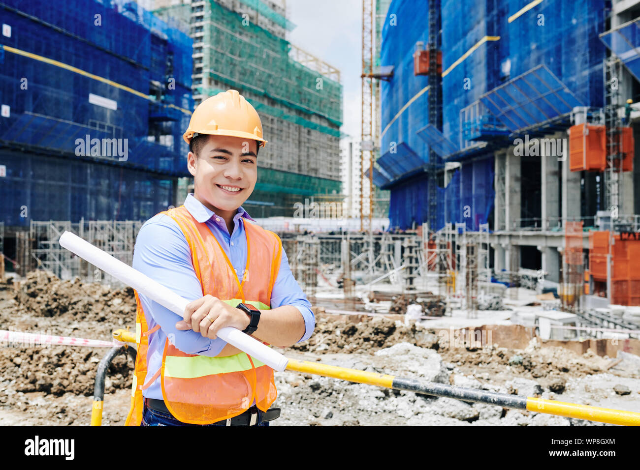 Portrait von fröhlichen selbstbewussten jungen vietnamesischen Techniker stehen auf der Baustelle mit Blättern Stockfoto