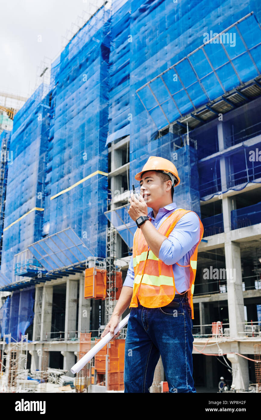 Junge vietnamesische Kopf Techniker sprechen über Walkie-talkie und geben Bestellungen an die Arbeiter auf der Baustelle Stockfoto