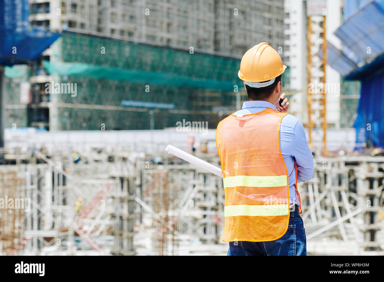 Ansicht der Rückseite des Professional Engineer in orange Weste mit Walkie-talkie-Mitarbeiter zu erklären, was zu tun ist Stockfoto