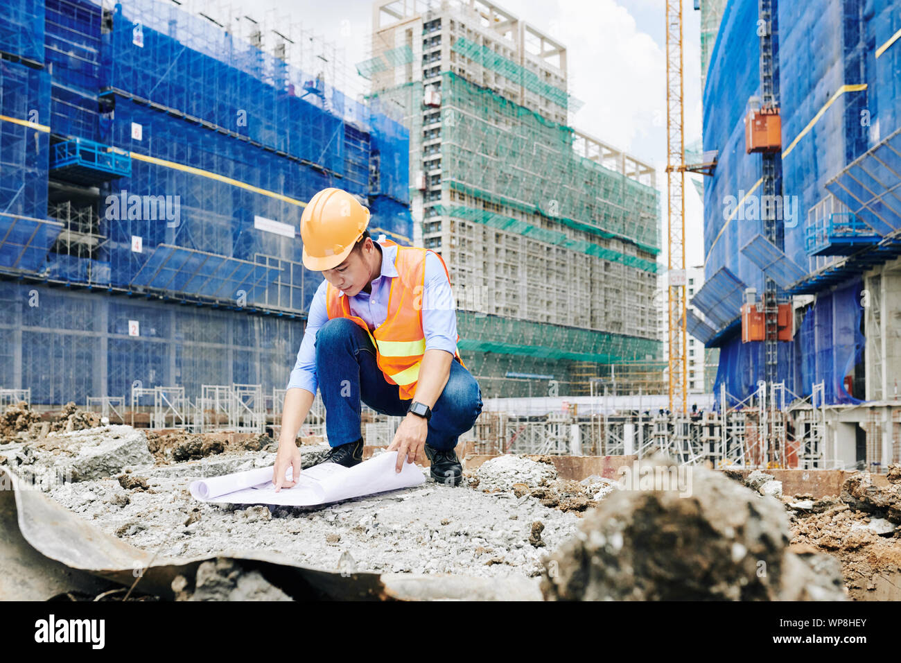 Asiatische Bauingenieur in orange Weste und hardhat zeigen auf Gebäude Plan beim Arbeiten im Freien an Constrution site Stockfoto