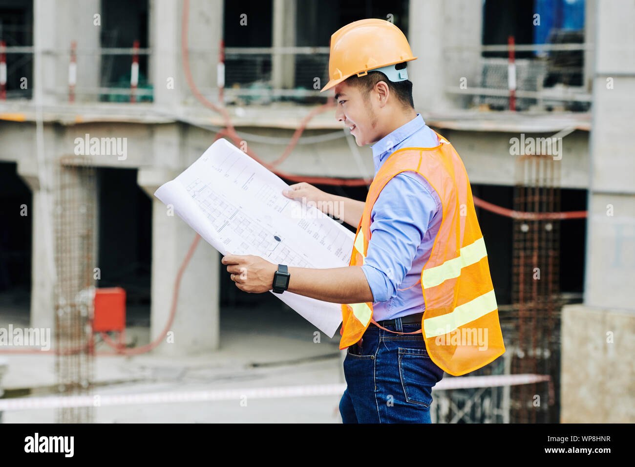 Lächelnd vietnamesischen Meister Prüfung Blaupause des neuen Gebäudes in seinen Händen, wenn auf der Baustelle arbeiten Stockfoto