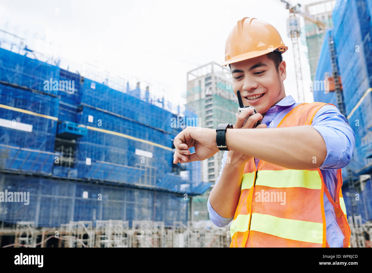 Lächelnd vietnamesischen Unternehmer im Gespräch mit Mitarbeitern über Walkie-talkie, und stellen Sie sicher, dass alles zur rechten Zeit getan werden, Stockfoto