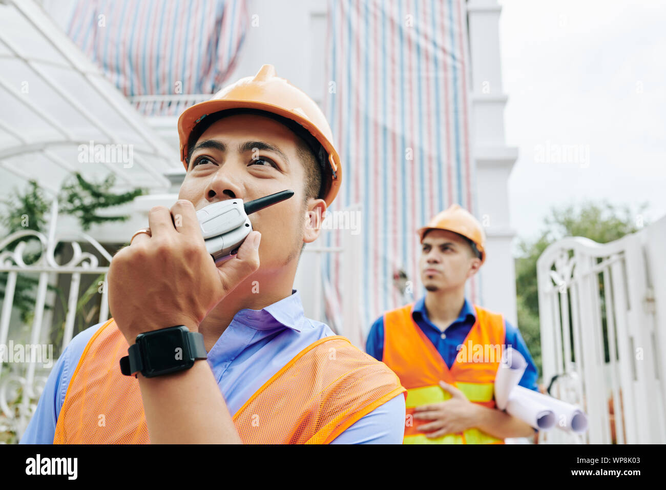 Schweren asiatischen Auftragnehmer controlling Arbeiten auf der Baustelle durch das Reden über walkie-talkie mit Kollegen Stockfoto
