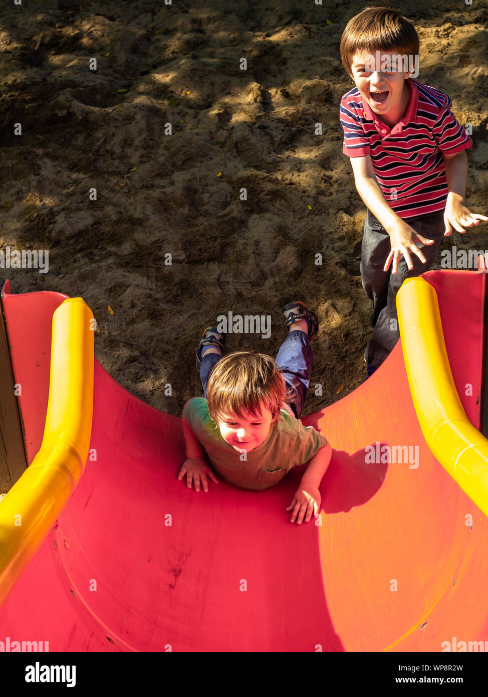 Ein Kleinkind Rutschen rückwärts hinunter eine Rutschbahn auf dem Bauch,  während seine älteren Kindergarten-alter Bruder lacht Stockfotografie -  Alamy