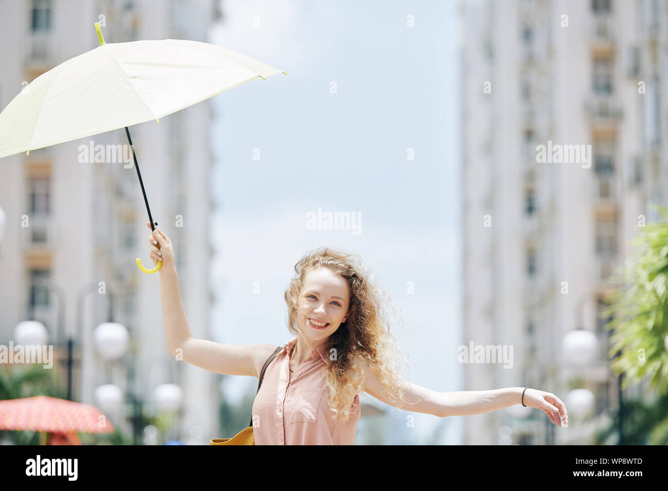 Glückliche junge hübsche Frau, die zu Fuß auf der Straße mit Regenschirm in der Hand auf windigen Tag Stockfoto