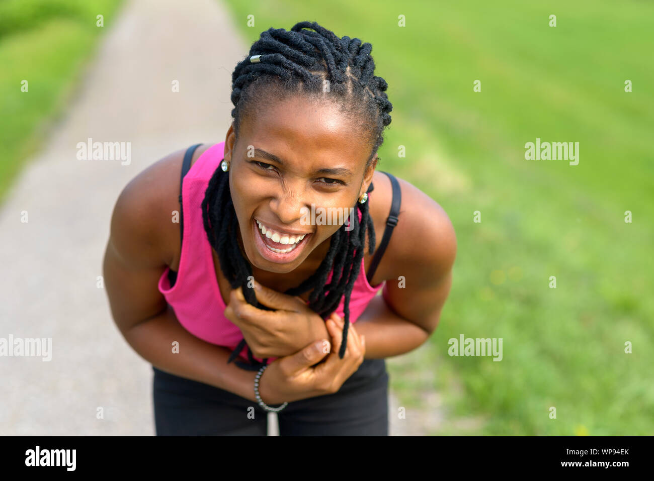 Sportliche junge afrikanische Frau nach vorne biegen lachend in die Kamera, als sie eine Pause dauert vom Joggen auf einem ländlichen Fußweg Stockfoto