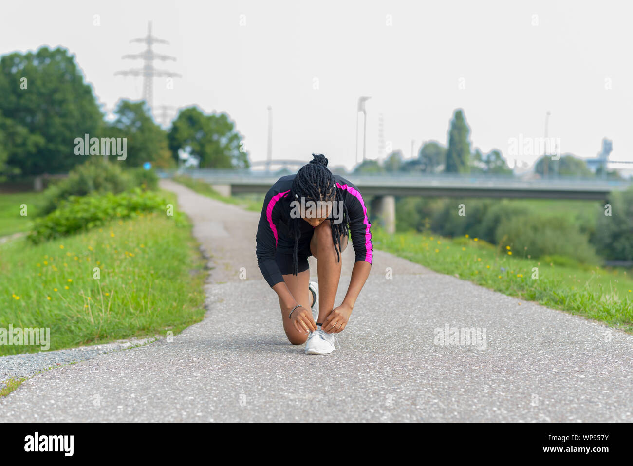 Afrikanische Frau anhalten Ihre Schnürsenkel zu binden, während Joggen entlang einer ländlichen Straße neben einem Fluss in einem Gesundheit und Fitness Concept Stockfoto