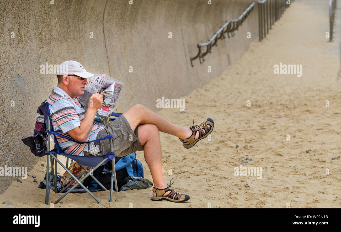 Ein Mann am Strand und eine Zeitung lesen. Stockfoto