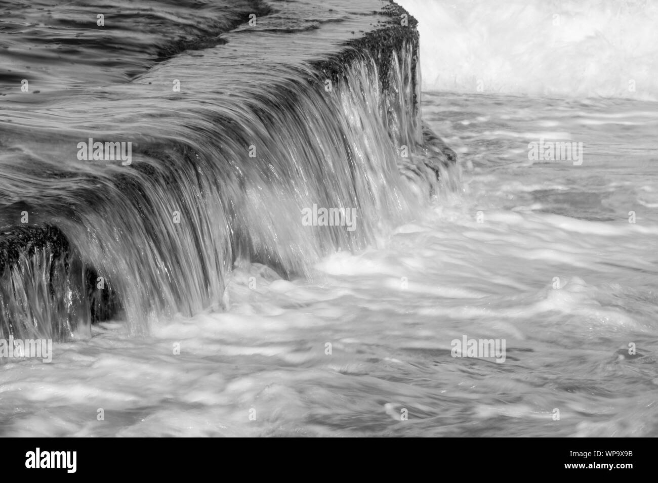 Schwarze und Weiße abstrakte Fotografien einer Meereslandschaft mit starken Rückspülen mit Wasser fließt über eine Flutwelle pool Wand auf einem niedrigen Verschlusszeit - leistungsstark Stockfoto