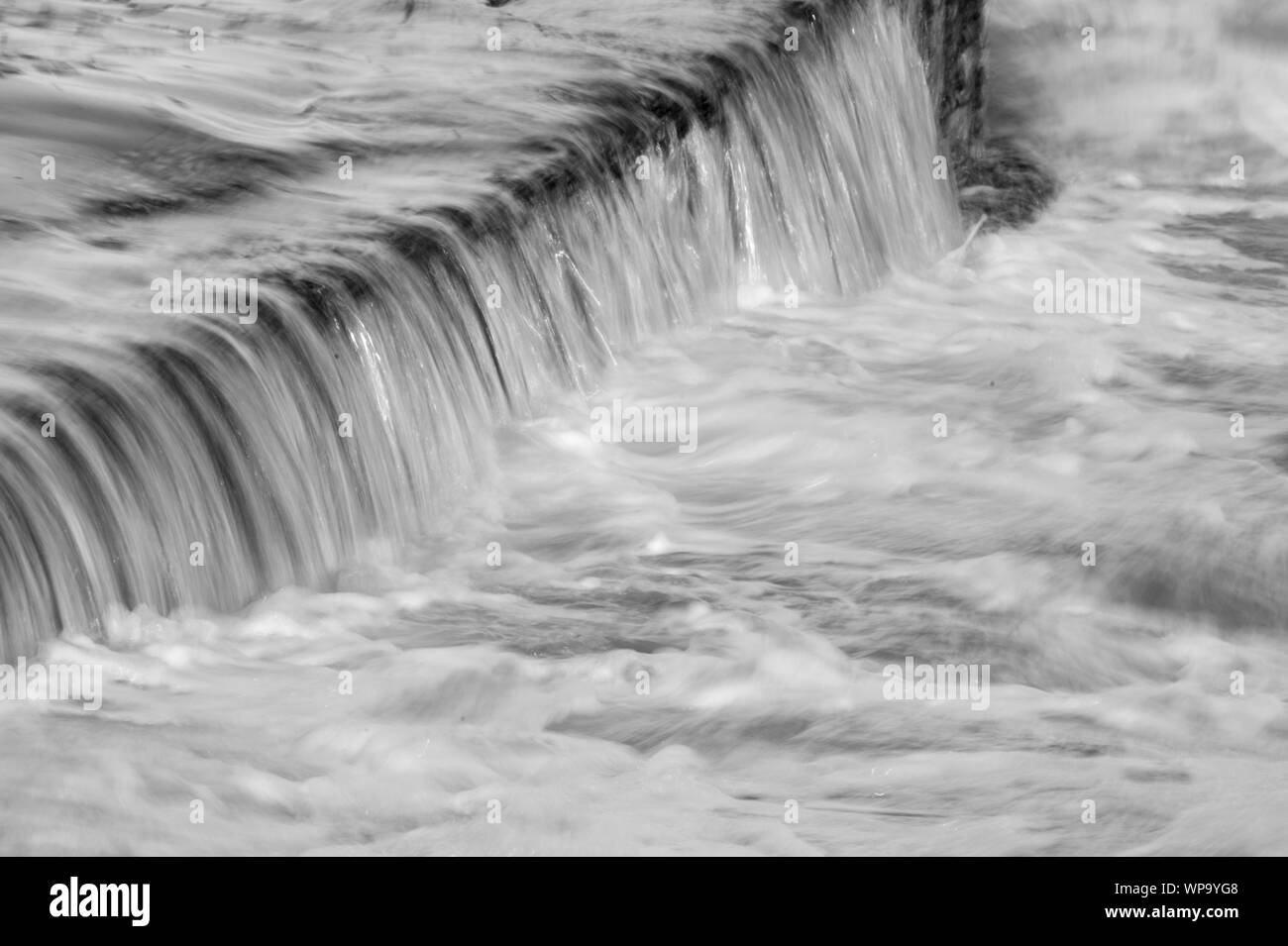 Schwarze und Weiße abstrakte Fotografien einer Meereslandschaft mit starken Rückspülen mit Wasser fließt über eine Flutwelle pool Wand auf einem niedrigen Verschlusszeit - leistungsstark Stockfoto