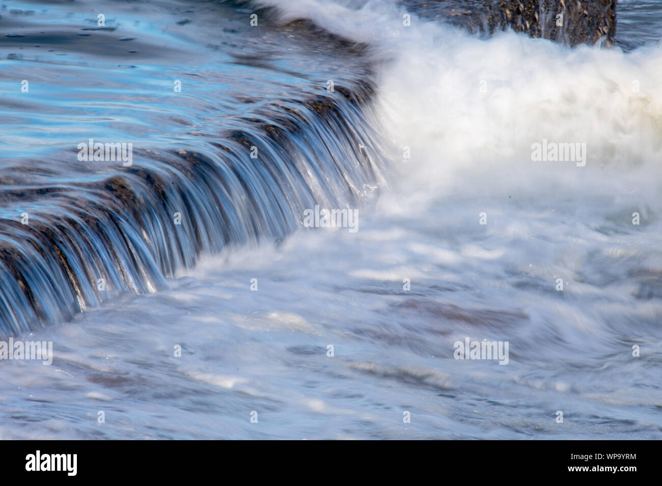 Starke Nachmittag, eingehende Flut mit Wellen, die auf eine Flutwelle pool Wand- und die Schaffung eines leistungsfähigen Überlauf schäumenden Brandung als Nachwirkung Absturz Stockfoto