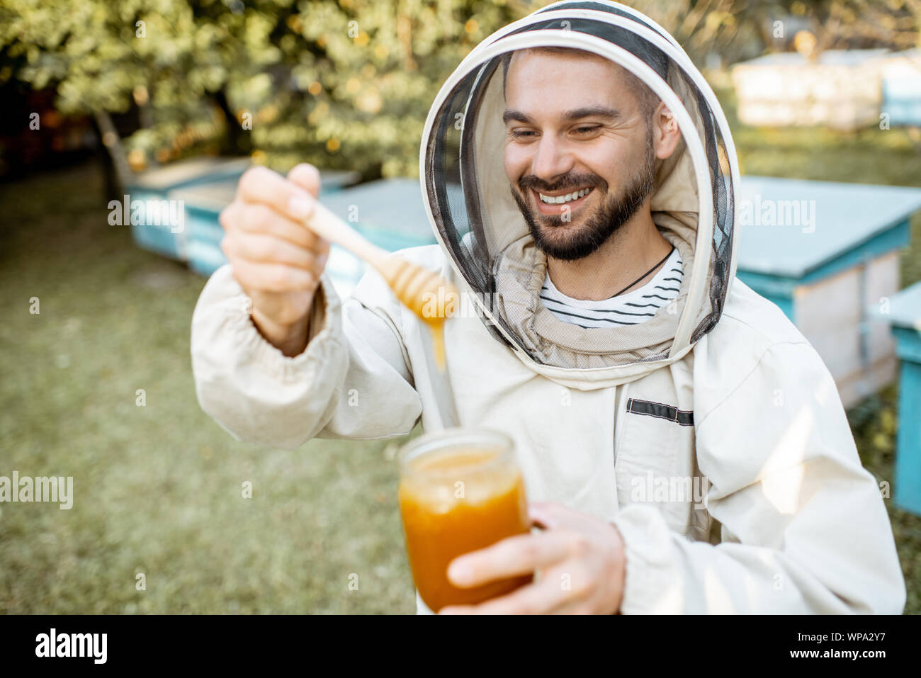 Porträt einer stattlichen beekeper in Schützende Uniform stehend mit Honig, Weinprobe, frisches Produkt auf die Imkerei im Freien Stockfoto