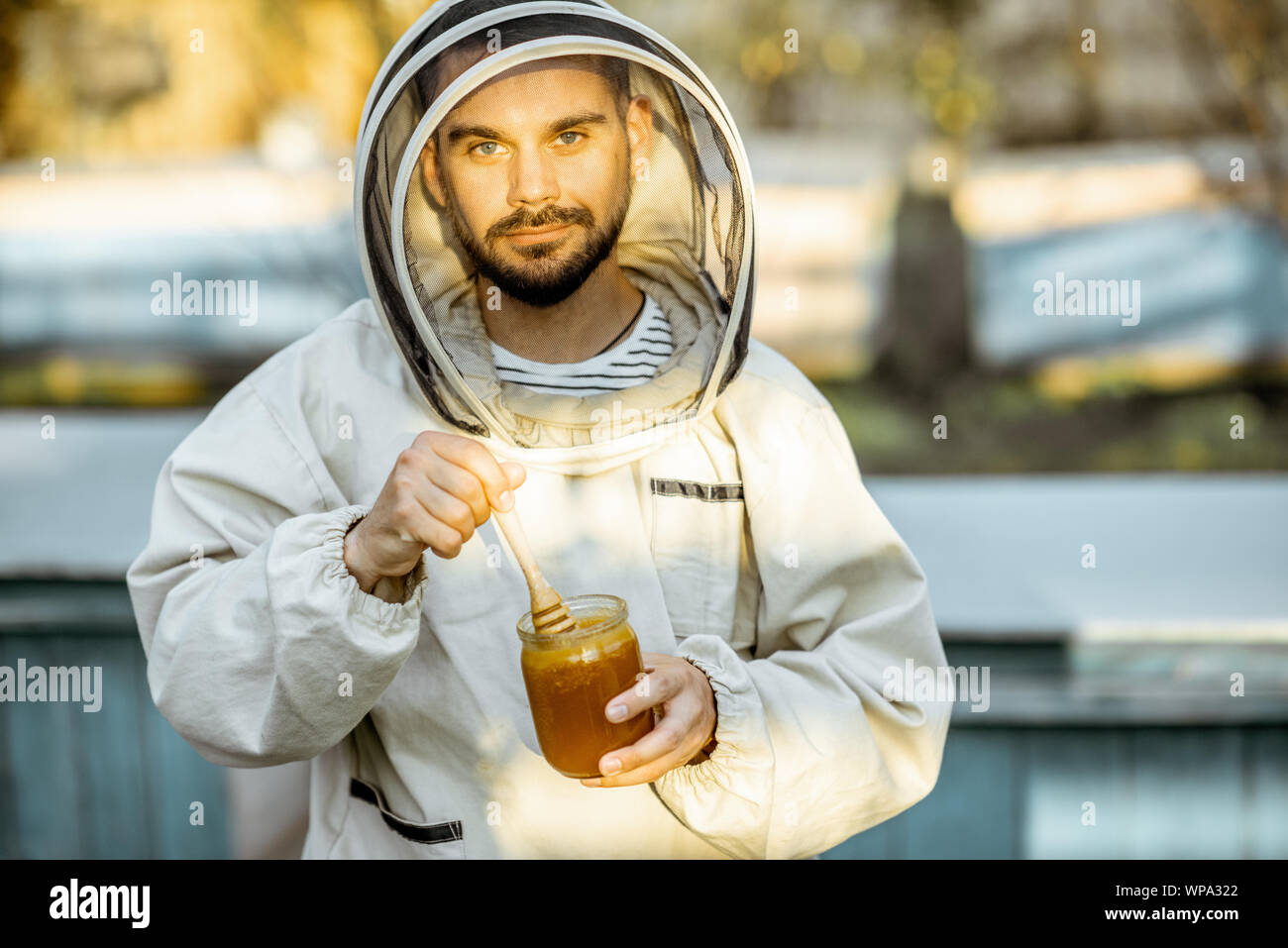 Porträt einer stattlichen beekeper in Schützende Uniform stehend mit Honig, Weinprobe, frisches Produkt auf die Imkerei im Freien Stockfoto