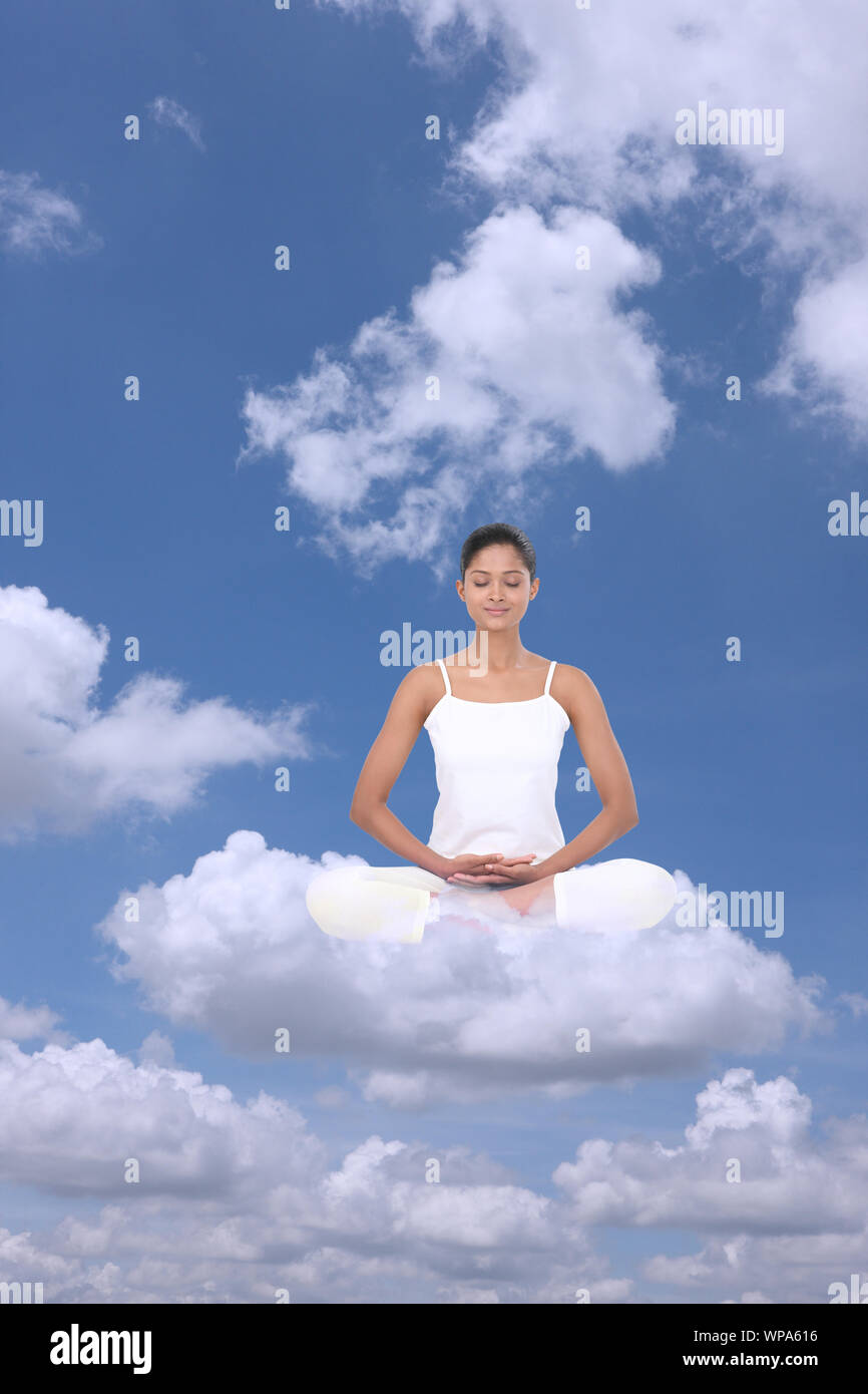 Junge Frau, die auf Wolken sitzt und Yoga praktiziert Stockfoto